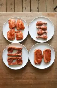 Top view of uncooked different meat fillet and steaks with drumsticks and ribs with seasoning on white plates placed on wooden table